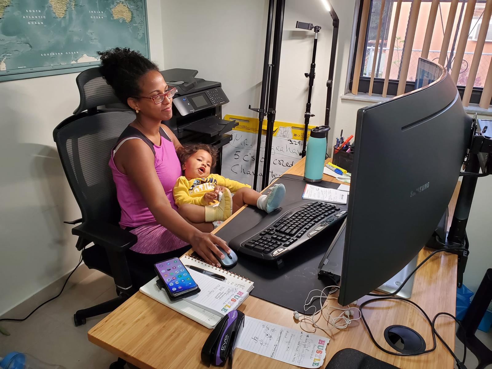 Yasnay at her desk holding her infant son while working — the moment she decided to build the business differently